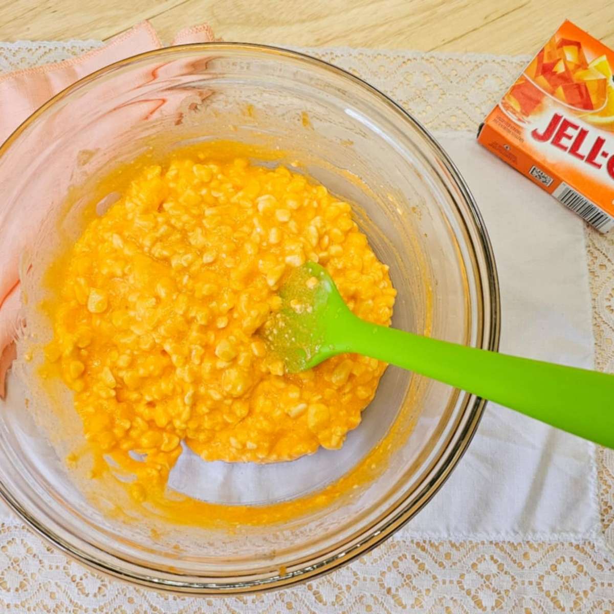 cottage cheese with orange jello mixed in, in a clear bowl on a vintage place mat with an orange jello package next to it