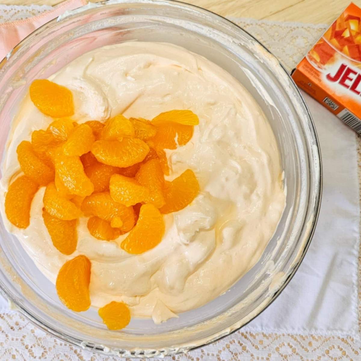 cool whip, cottage cheese and mandarins in a clear glass bowl with an orange jello package next to it