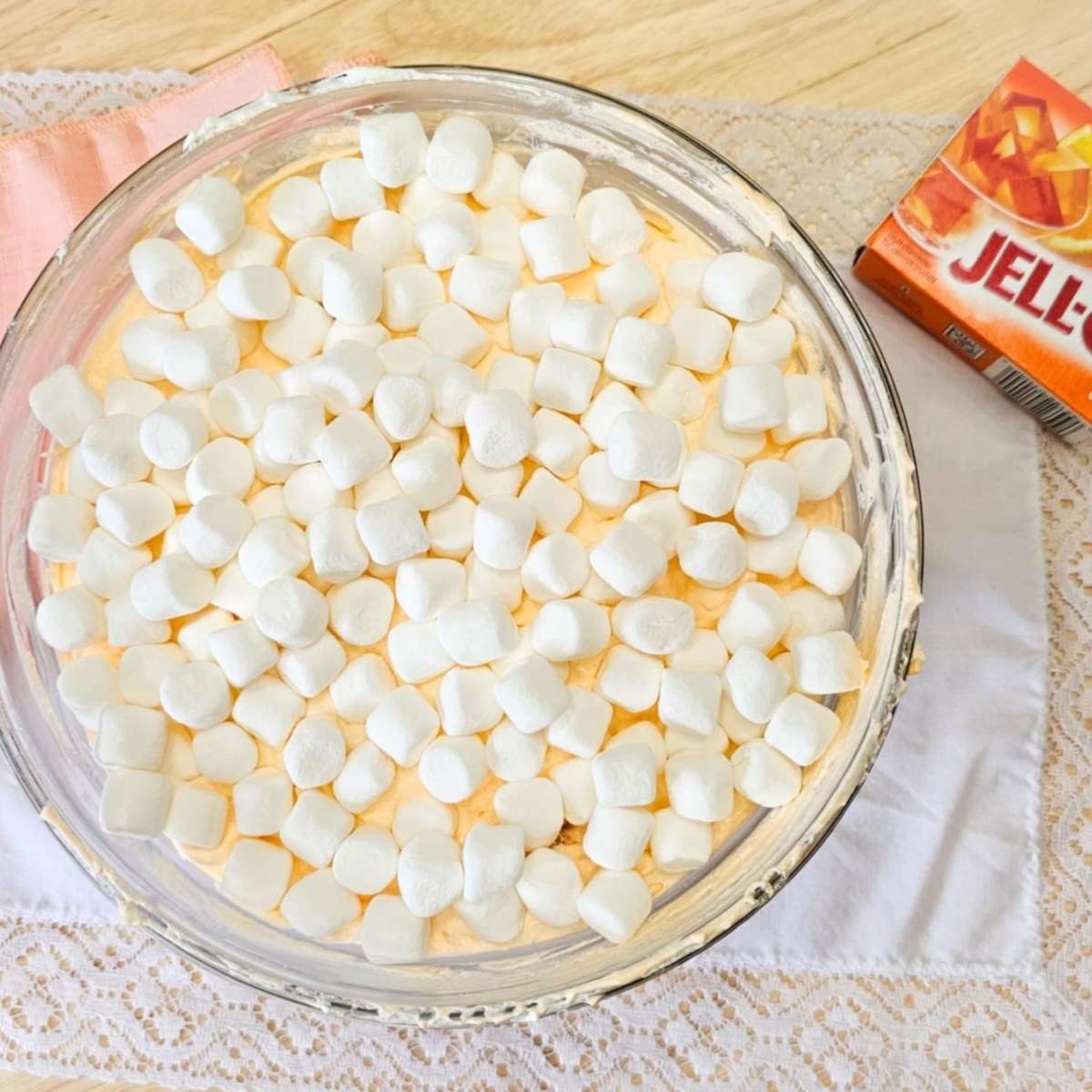 grandmas orange fluff dessert topped with mini marshmallows in a large bowl with an orange jello package next to it