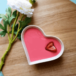Strawberry milk jello served in a white heart dish and garnished with a fresh strawberry