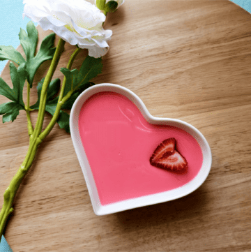 Strawberry milk jello served in a white heart dish and garnished with a fresh strawberry