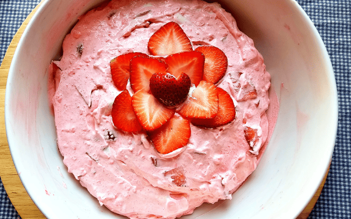 strawberry Jell-O fluff in a white bowl and topped with fresh strawberries in a flower pattern
