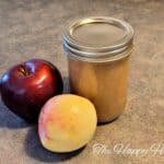 homemade apple sauce in a small mason jar with two different types of apples sitting to the side of it