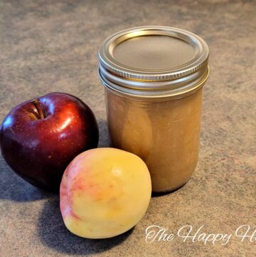 homemade apple sauce in a small mason jar with two different types of apples sitting to the side of it