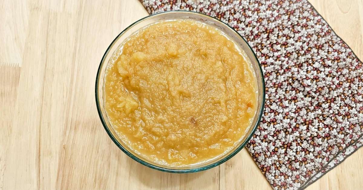 apple sauce in a clear glass bowl sitting on a fall cloth napkin on a wooden table