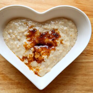 creamy oatmeal with brown sugar sitting in a white heart glass dish on a wooden cutting board