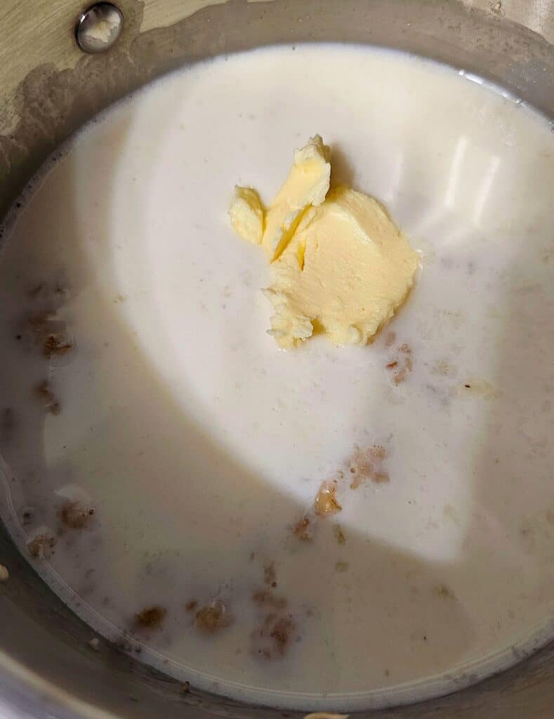 cooked oatmeal sitting in a stainless steel pot with milk, butter and sugar