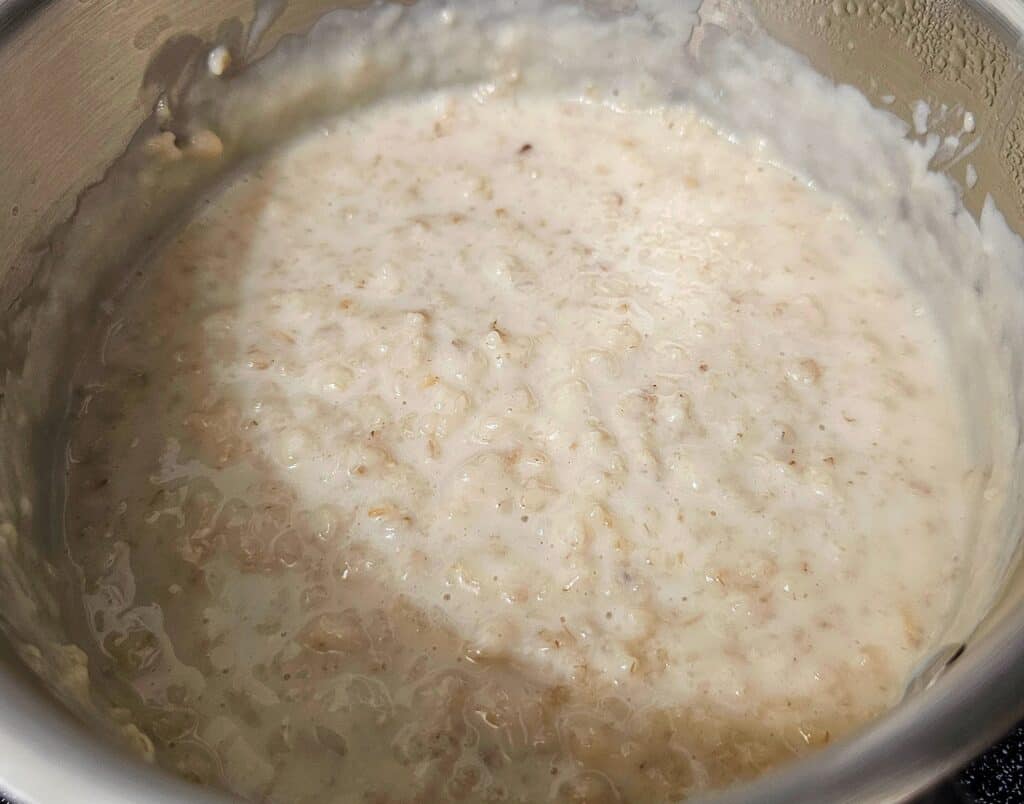 creamy oatmeal sitting in a stainless steel pot with heavy cream
