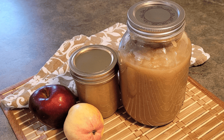 homemade apple sauce in 2 mason jars with2 apples to the side of them