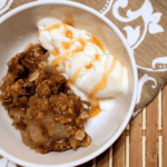 grandmas old fashioned apple crisp sitting in a white bowl with vanilla ice cream drizzled with caramel sauce