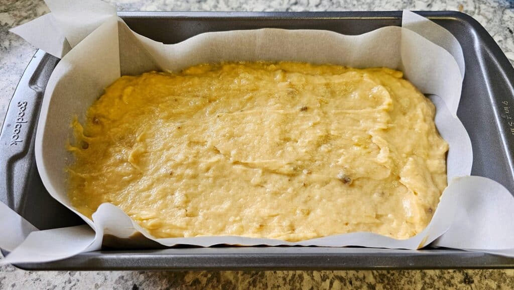 old fashioned banana bread sitting in a 9x5 parchment lined baking pan and ready to get baked in the oven