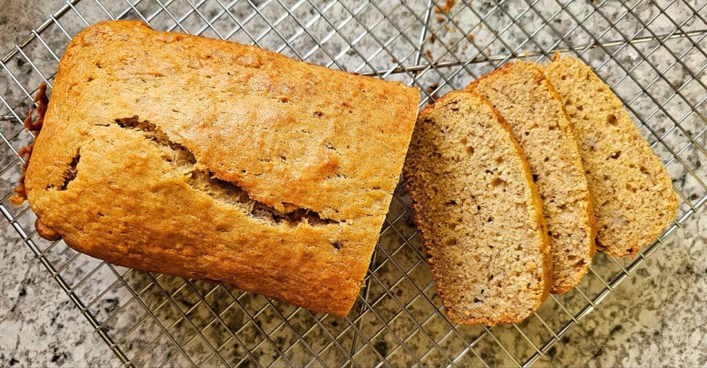 baked banana bread sitting on a cooling rack on a white and grey counter top