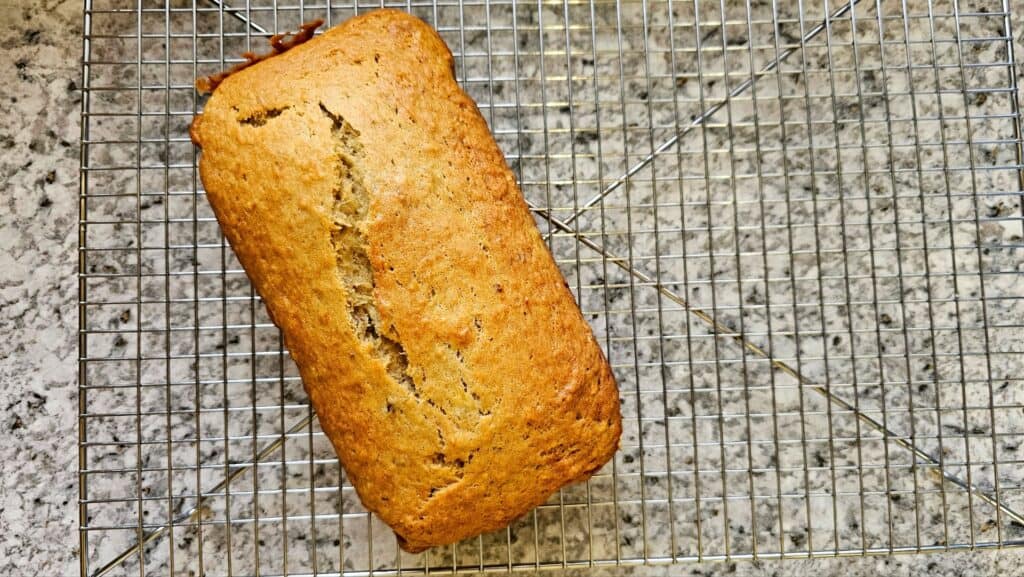 Baked banana bread sitting on a wire cooling rack on a grey and white counter top