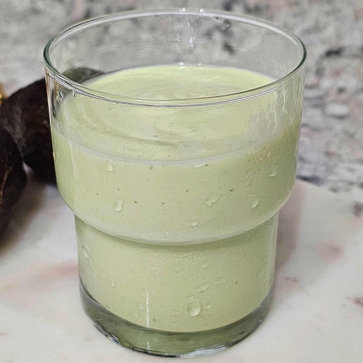 avocado smoothie in a clear glass on a marble dish