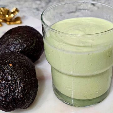Vietnamese avocado smoothie sitting on a marble board with gold handles with 2 fresh avocados next to the glass
