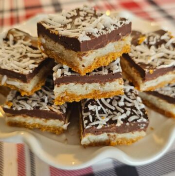 triple layer bars sitting on a vintage serving platter on a red, white and black plaid table cloth