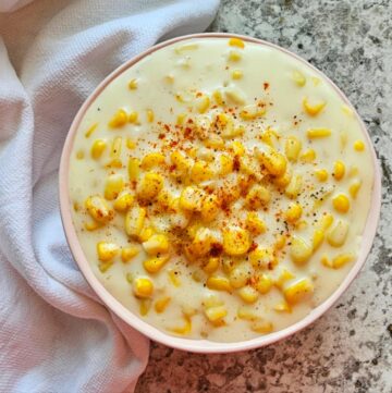 Easy Creamed Corn Recipe (Perfect Easter Side Dish) sitting in a pink bowl on a counter top with a dish towel to the side of it