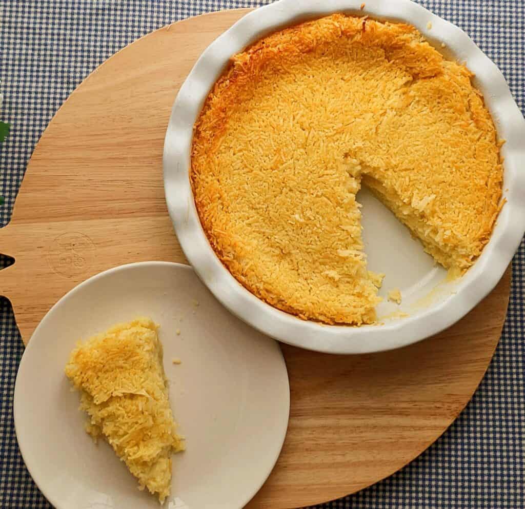 Impossible Coconut Pie Recipe (without bisquick) sitting on a blue and white checkered table cloth and wooden cutting board in a ceramic pie dish