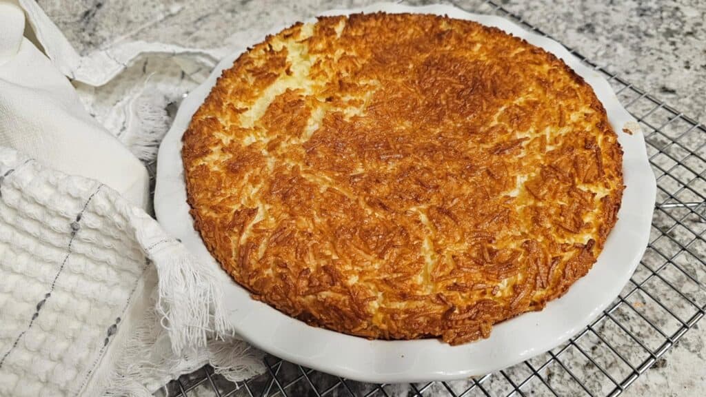 Impossible Coconut Pie Recipe (without bisquick) sitting on a cooling rack with a hand towel next to it that is white and grey