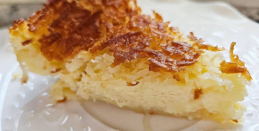 a slice of Impossible Coconut Pie Recipe (without bisquick)  sitting on a white ceramic dish