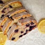 glazed blueberry lemon bread siting on parchment paper with sliced lemons on the sides of it
