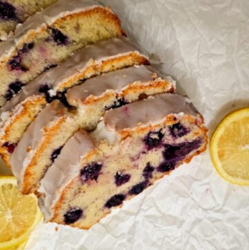 glazed blueberry lemon bread siting on parchment paper with sliced lemons on the sides of it