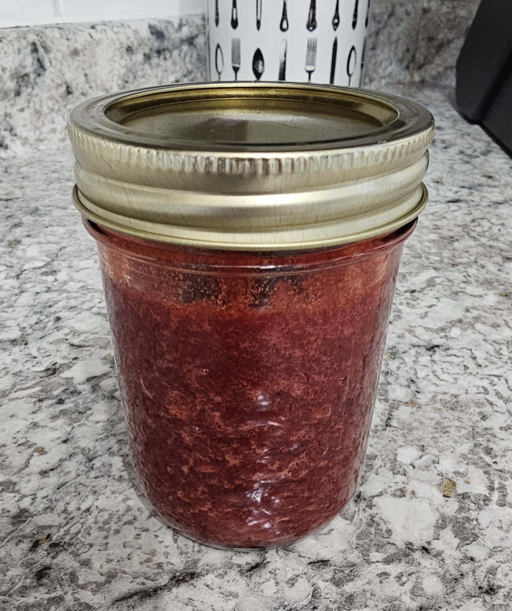 Strawberry Jam in a mason jar on a white counter with grey and black designs on it