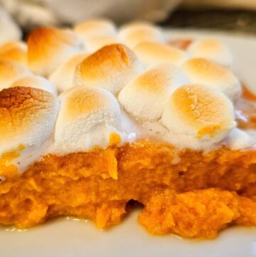 a slice of sweet potato casserole sitting on a white plate that has toasted marshmallows on top