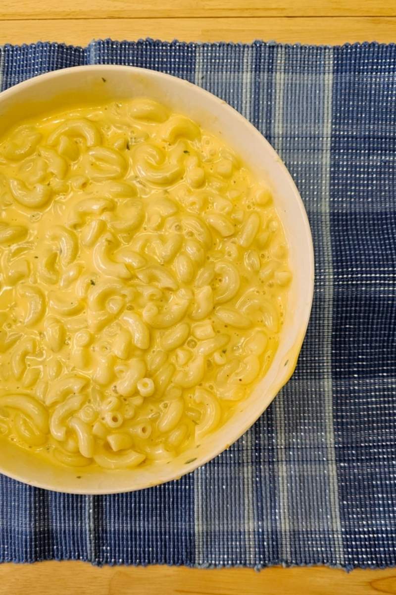 creamy macaroni and cheese in a white glass bowl sitting on a blue place mat