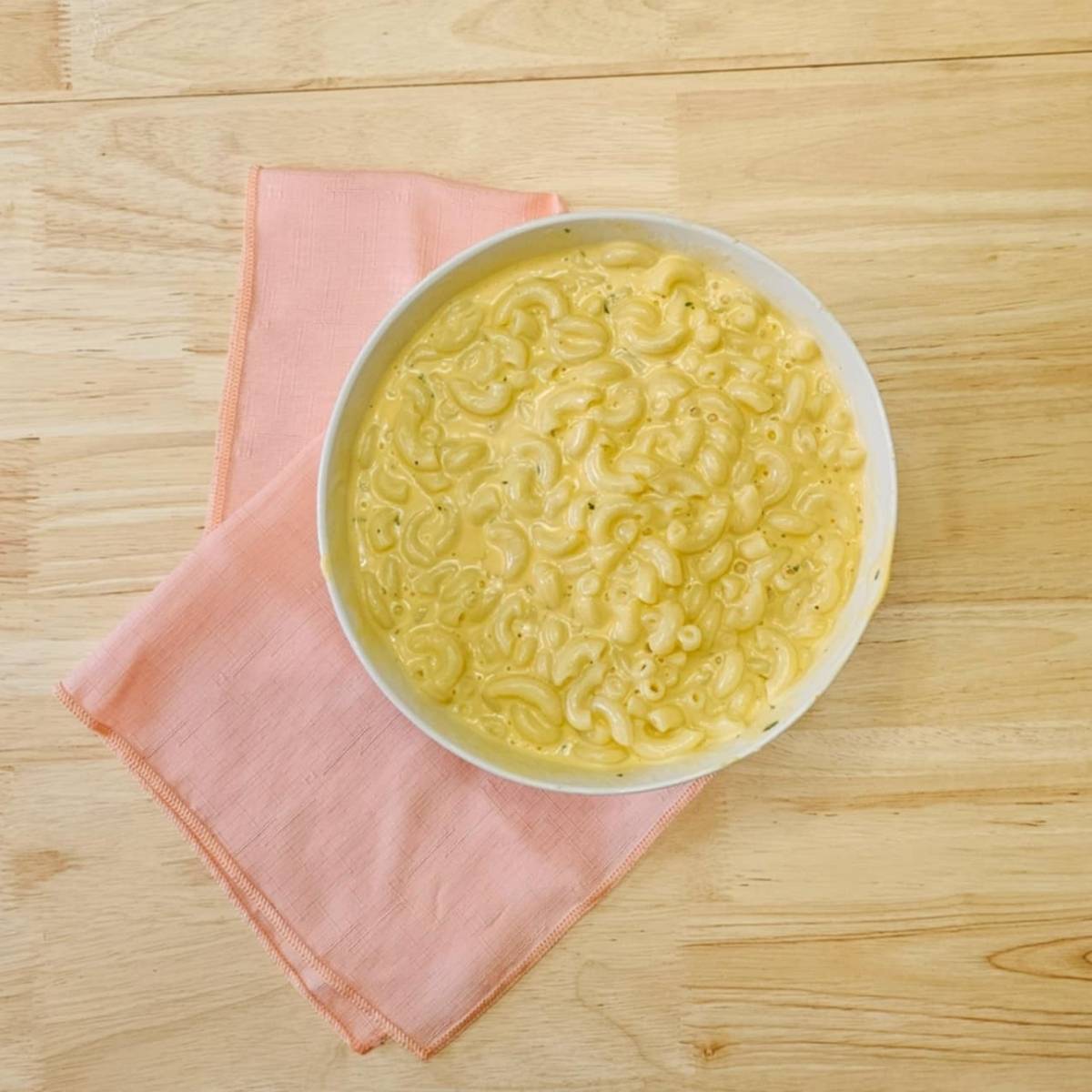 macaroni and cheese on a wooden counter top with a pink cloth napkin under it