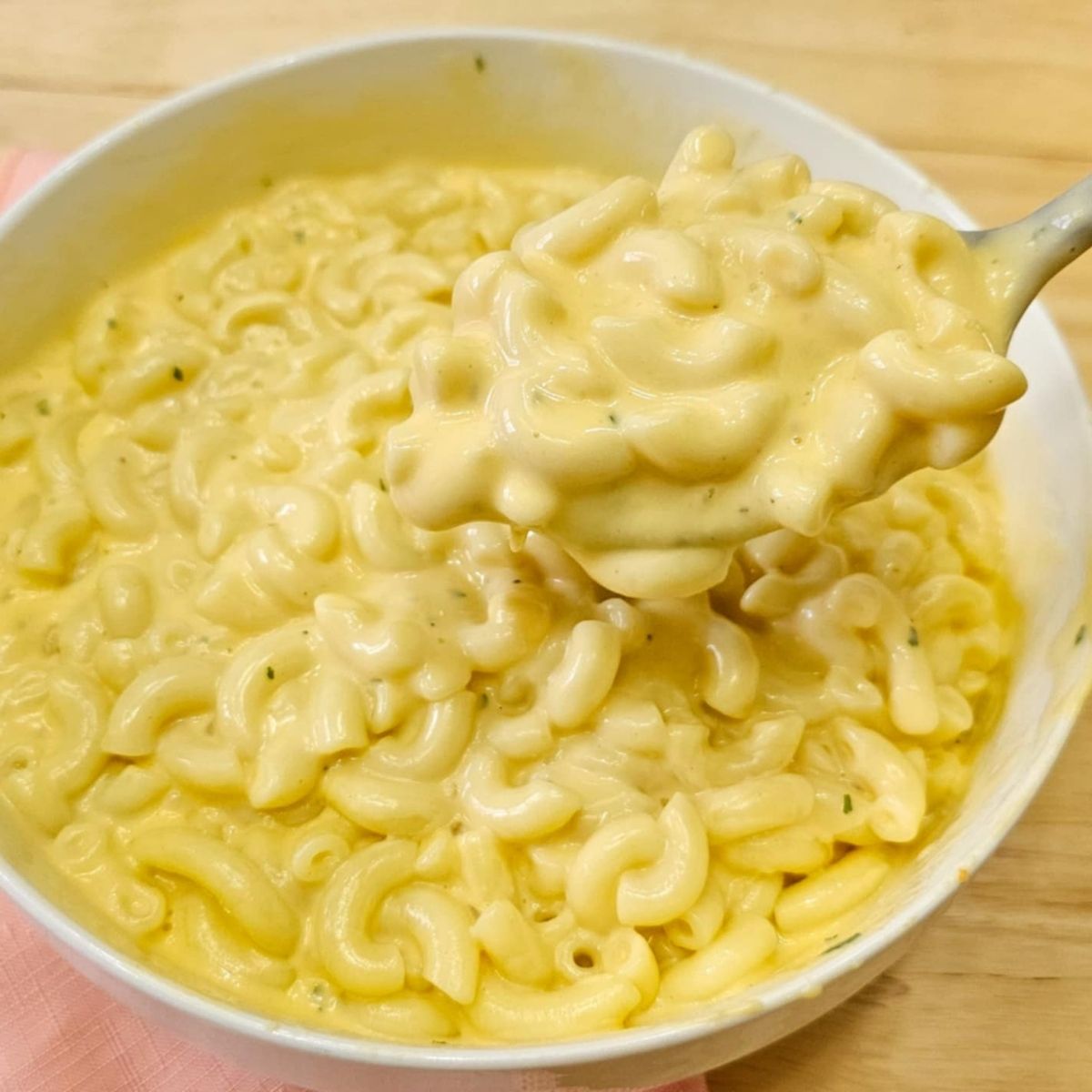 creamy macaroni and cheese in a large white bowl being scooped out by a spoon