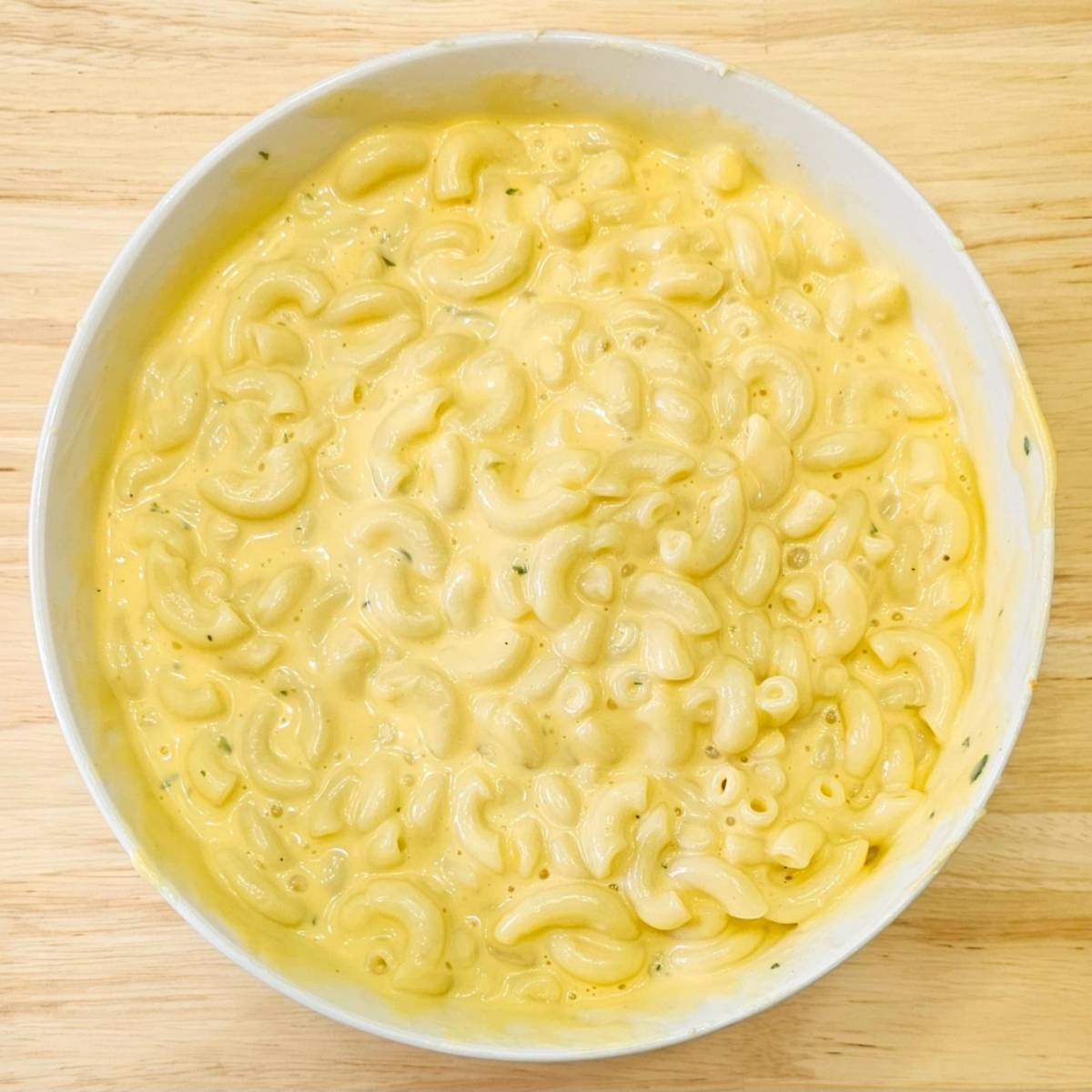 creamy macaroni and cheese in a white bowl on a wooden counter top