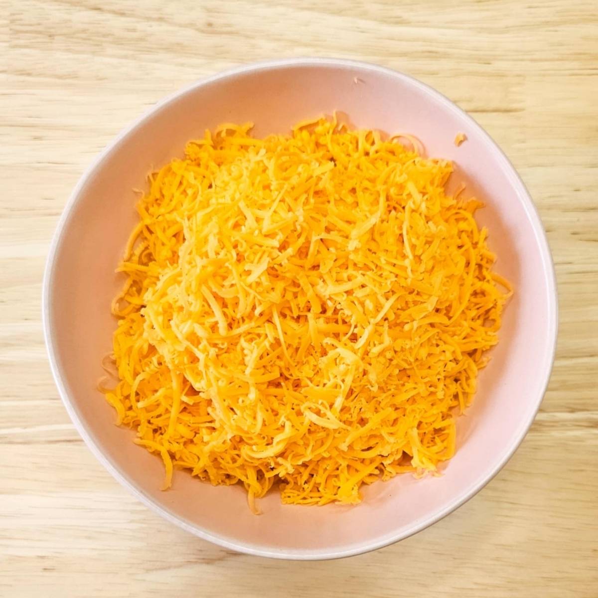 cheese, shredded fine in a pink bowl on a wood counter