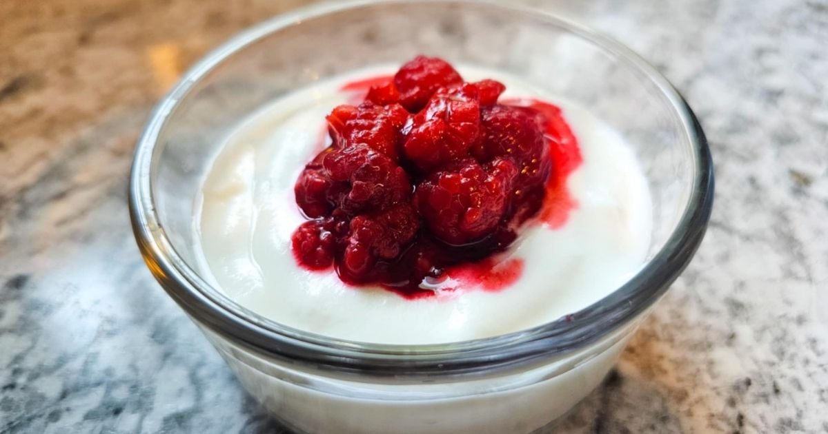 homemade yogurt in a glass bowl topped with raspberries