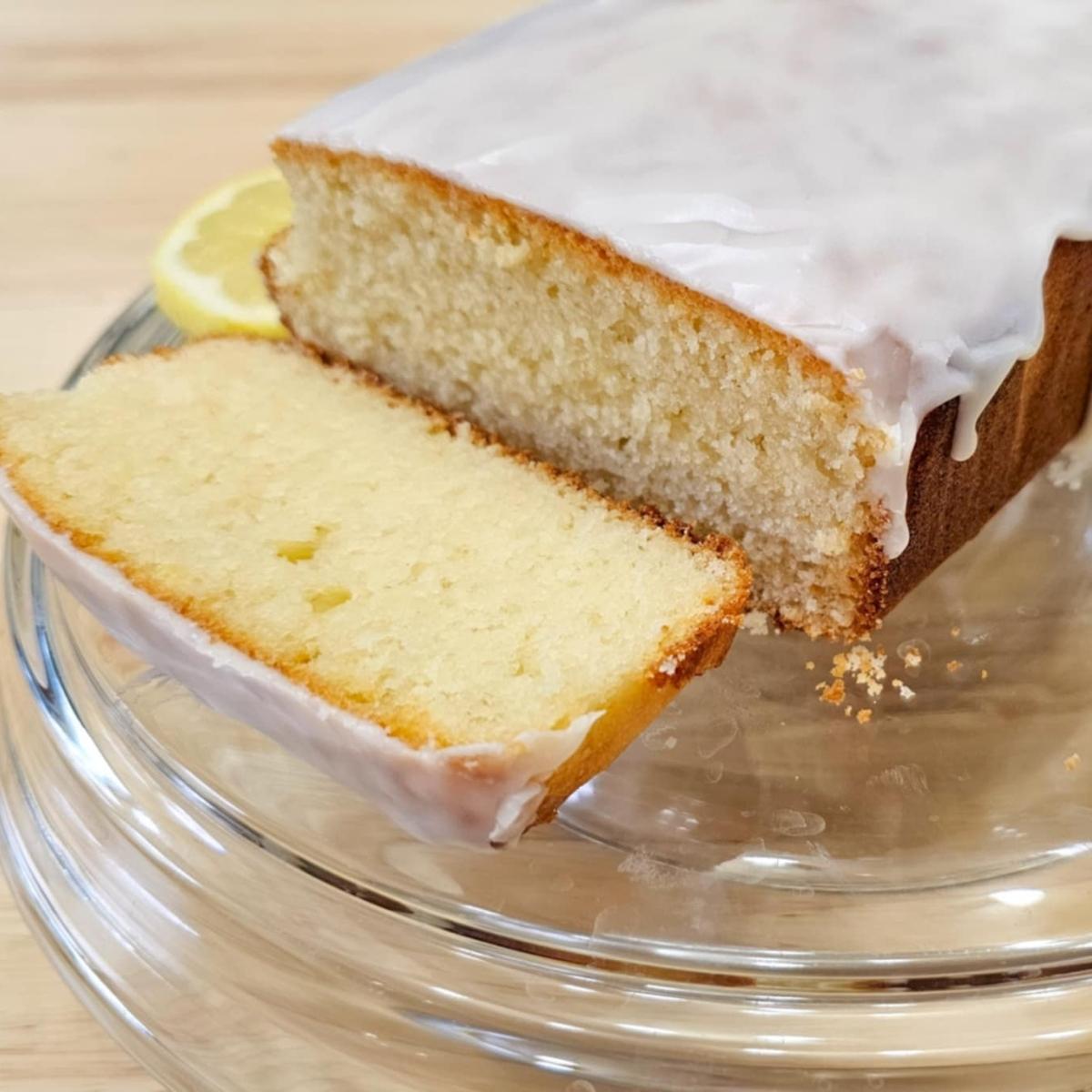 glazed loaf on a cake dish with a slice of lemon next to it