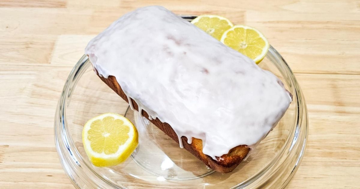 lemon loaf on a cake dish with freshly sliced lemons surrounding it