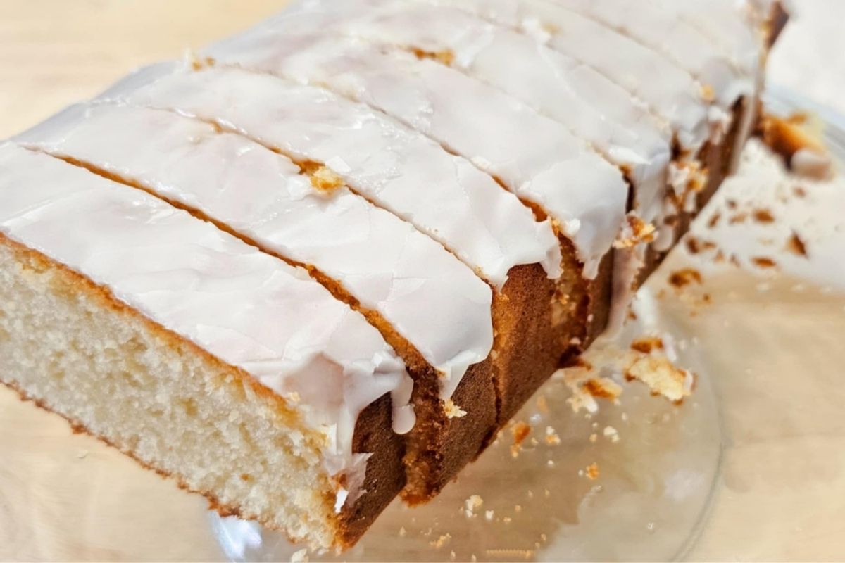 sliced glazed lemon loaf on a serving platter with crumbs from the loaf next to it