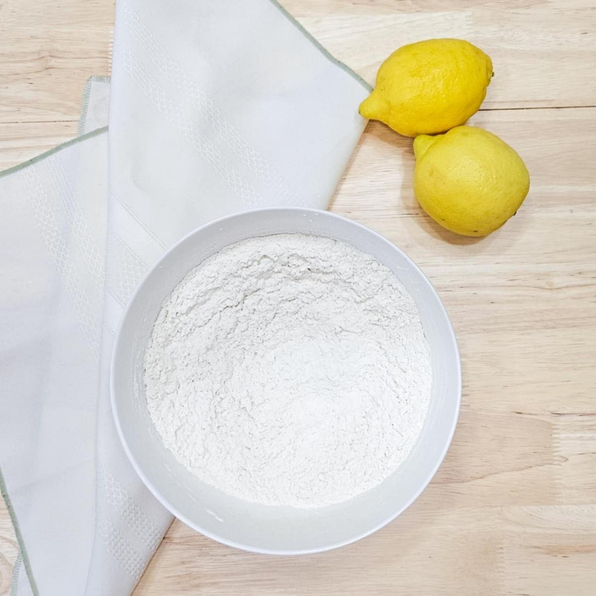 flour, baking powder and salt in a bowl with 2 lemons next to it