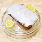 lemon loaf on a glass serving platter with sliced lemons next to it