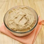 honey cinnamon butter in a glass bowl on a wooden counter on a peach cloth napkin