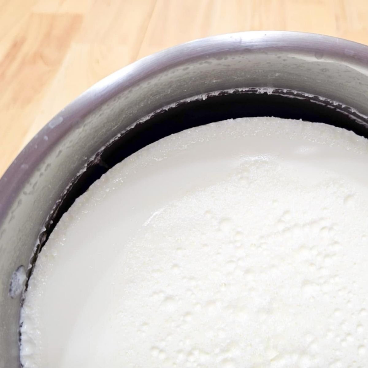 yogurt tilted in a pot to show that it is done as the yogurt has pulled from the sides
