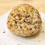 1950s cheese ball covered in chopped walnuts on a white plate thats sitting on a wooden counter top
