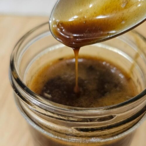 balsamic dressing in a mason jar being that has dressing being drizzled into it with a spoon