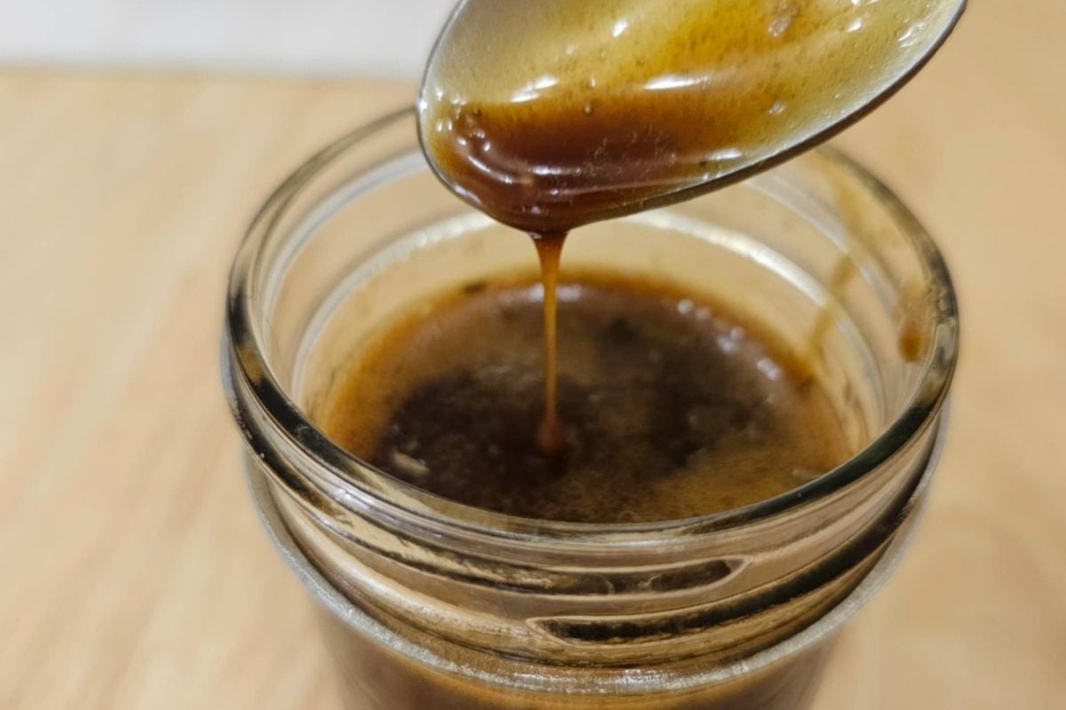 balsamic dressing in a mason jar being that has dressing being drizzled into it with a spoon