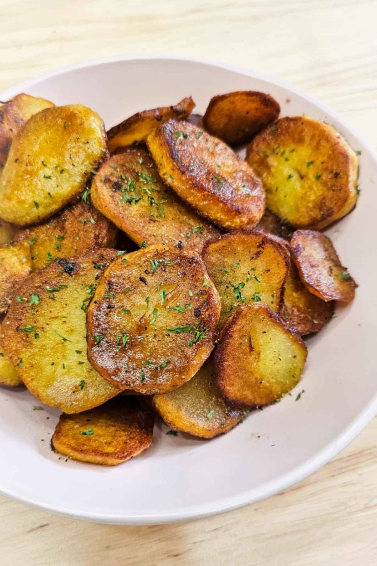 pan fried potatoes in a serving dish on a wooden counter top and garnished with parsley