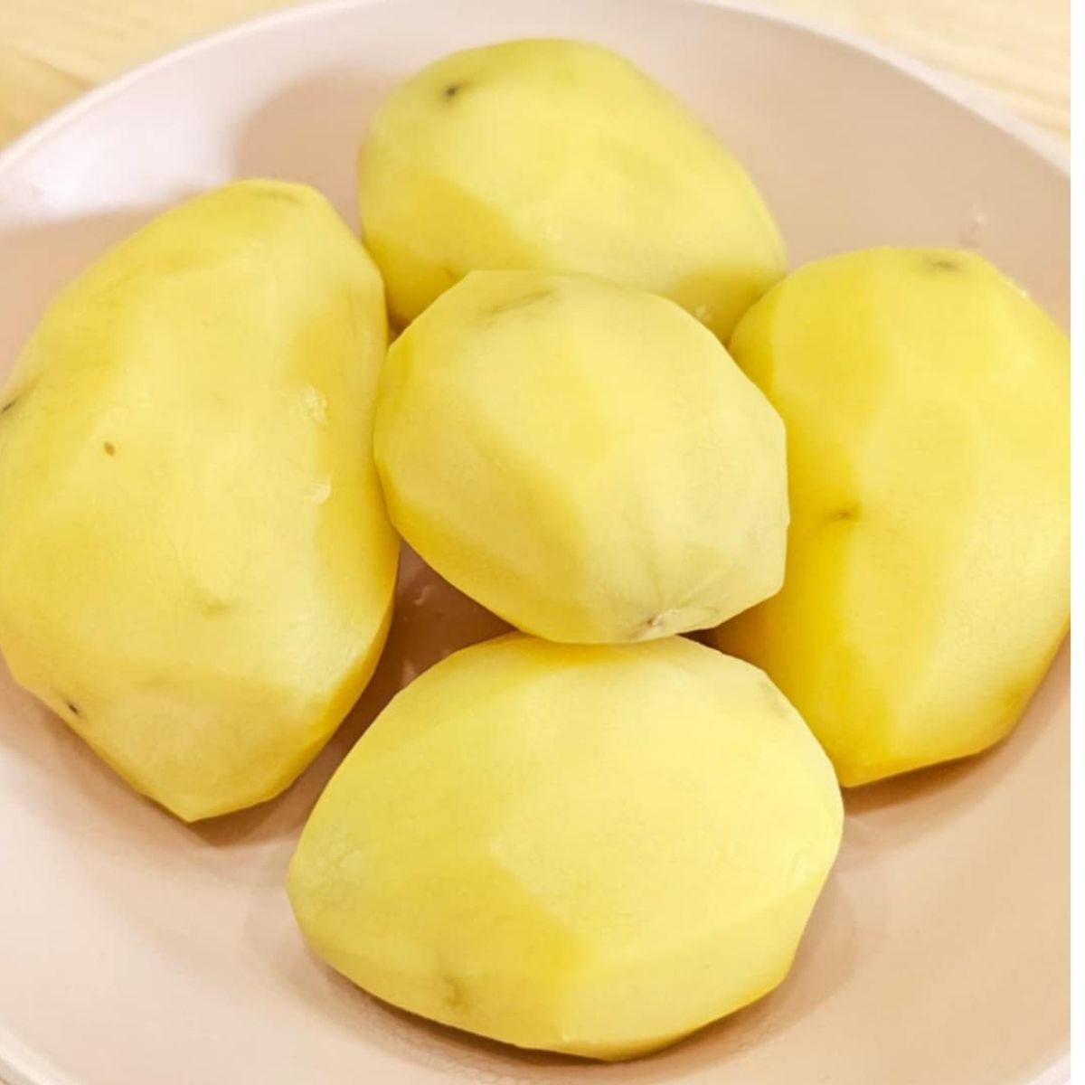 boiled and peeled potatoes sitting in a pink dish on a wooden counter top