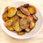 pan fried potatoes in a pink serving dish on a wooden counter and garnished with parsley