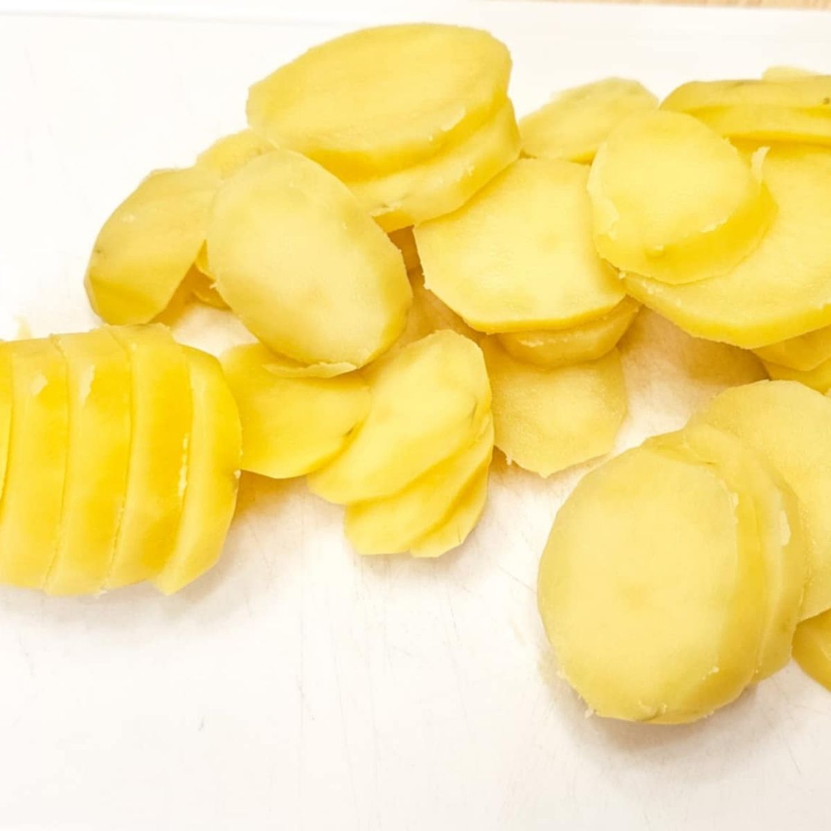boiled and sliced potatoes sitting on a white cutting board