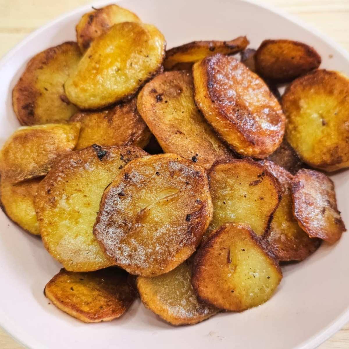 Sliced and pan fried potatoes sitting in a pink bowl getting ready to be served