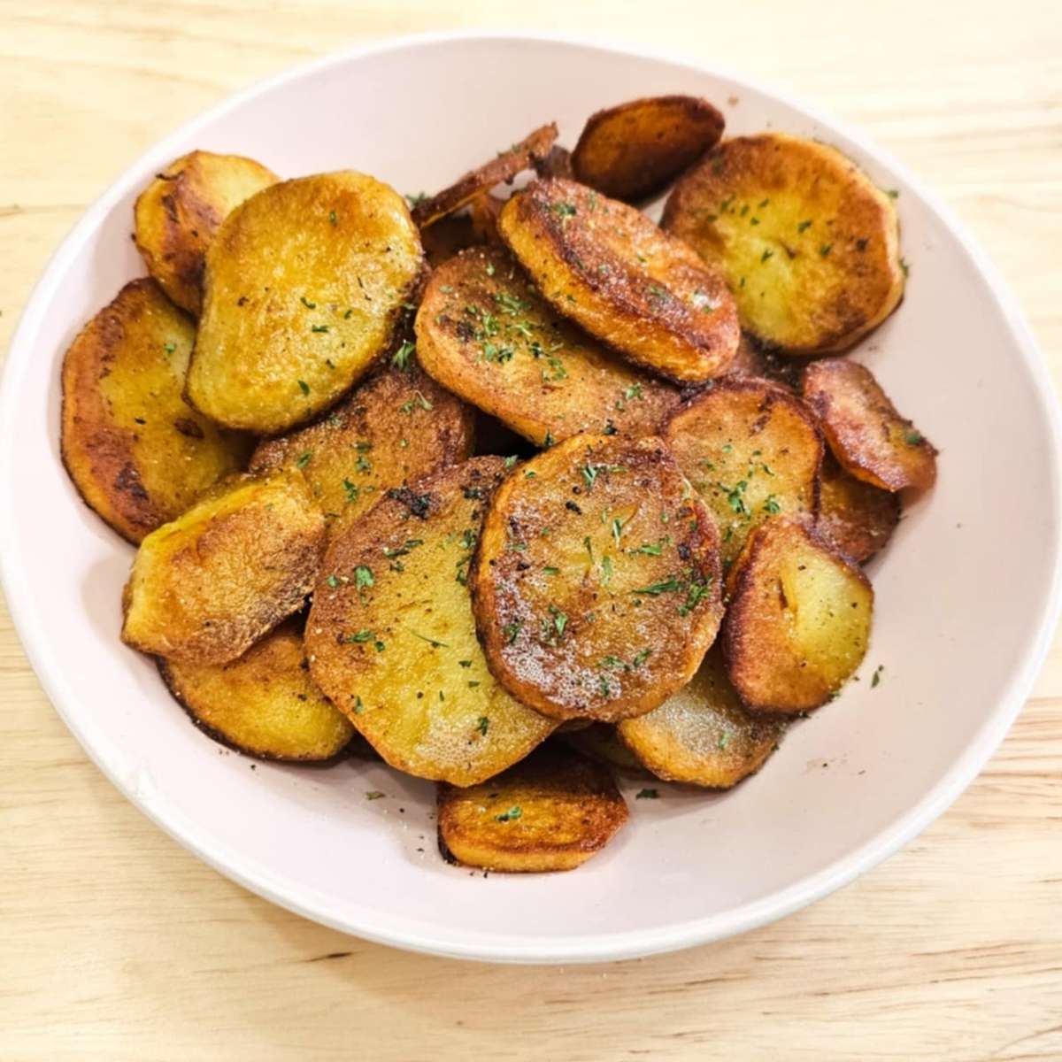 pan fried potatoes in a pink serving dish on a wooden counter and garnished with parsley